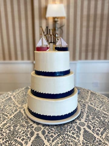 Three-tier white cake banded with navy ribbon and a gold topper