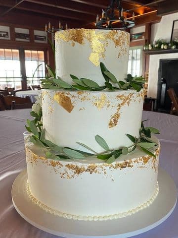 Two-tier white cake with fresh greenery and gold leaf