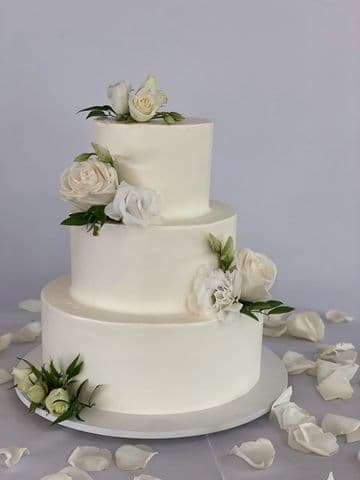 Three-tier white wedding cake with white roses and greenery