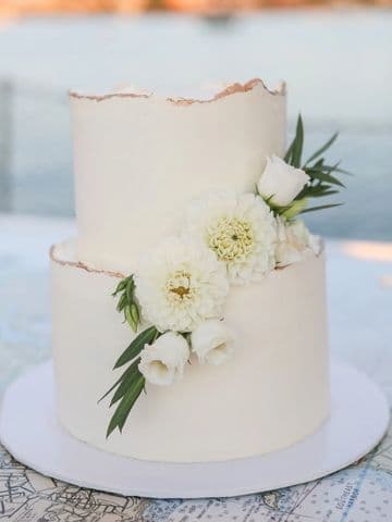 Blush two-tier wedding cake with white flowers and a gold rim